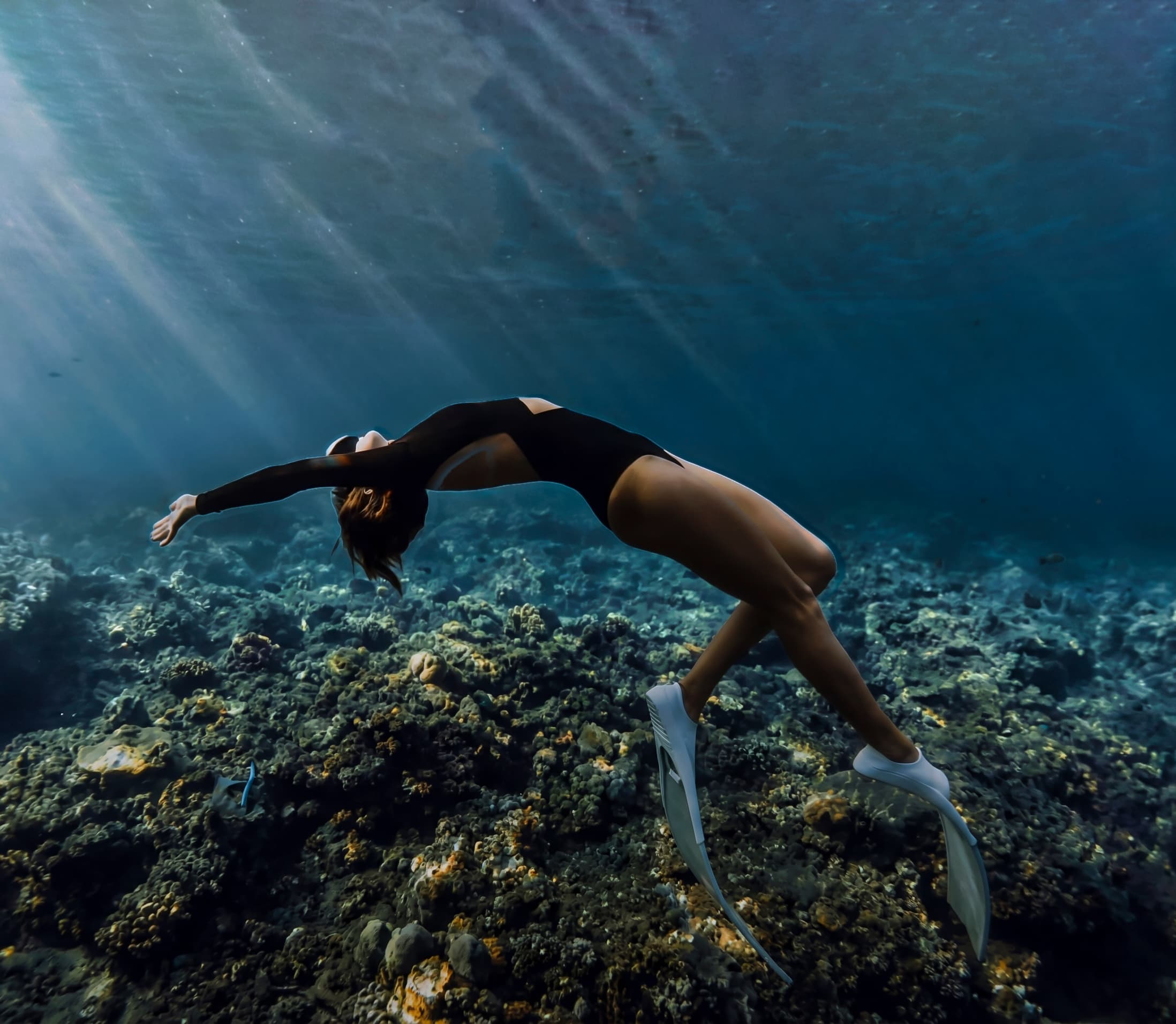 Freediver descending along a reef in open water