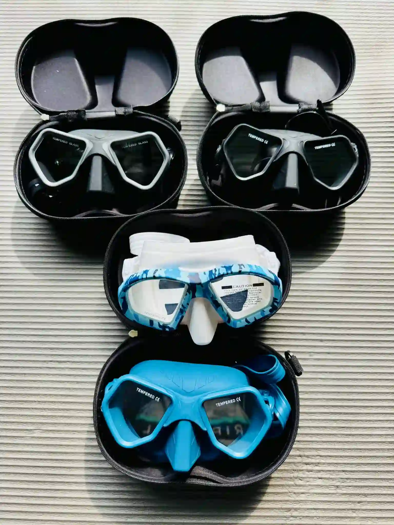 Collection of freediving masks in cases, in black, blue camouflage, and light blue colorways